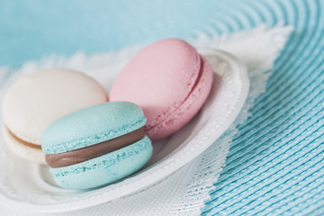Three macaroons of different colors and different tastes in a white plate, white napkin.