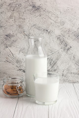 Bottle of almond milk with glass and almonds in jar on rustic white wooden table. Vertical orientation