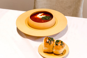 red soup with rolls on white table