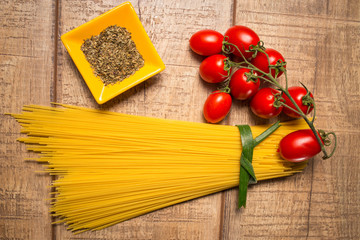 Spaghetti and Roma tomatoes isolated on wood table background. Uncooked Italian dried spaghetti. Top view. Flat lay.