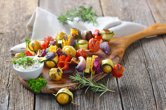 Vegetarisch grillen: Bunte  Gem&uuml;sespie&szlig;e vom Grill mit Kr&auml;uterdip  - Grilled skewers with mixed vegetables served  on a wooden cutting board with a vegan herb dip