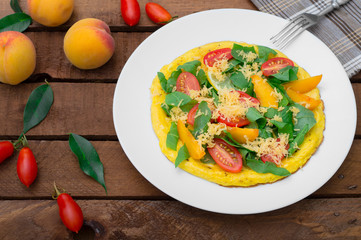 Frittata with peach, vegetables and cheese in a white plate on the rustic wooden background. Top view