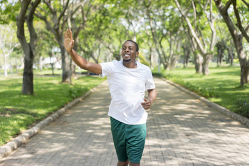 Friendly sporty black guy jogging in city park and greeting familiar sportsmen. Young Afro American...