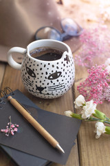 Black fragrant coffee, flowers, hat and glasses. Good morning . Women's accessories and notepad with a pen.