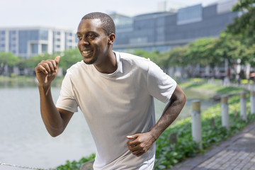 Joyful sporty black guy running by city pond. Young Afro American feeling runners high during morning run outdoors. Fitness and healthy lifestyle concept