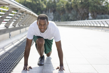 Tensed sporty black man in starting position ready to run on walkway. Young Afro American guy keeping fit and running in open air. Fitness and healthy lifestyle concept