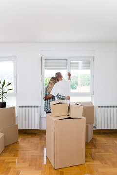 Happy Middle Aged Couple With Boxes Moving Into New Home Or Apartment. Real Estate Theme.