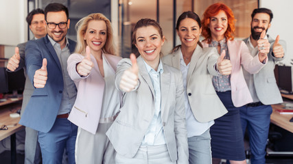 Successful business people with thumbs up looking at camera