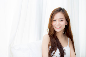 Naklejka premium Portrait beautiful young asian woman standing and smile the window at bedroom while wake up with sunrise at morning, lifestyle and relax concept.