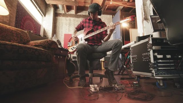 Bass Player Sitting in Recording Studio Move In. a wide angle view of a bass player sitting in a chair playing while camera moves in low angle in recording studio