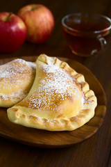 Chilean apple empanada with icing sugar, cup of tea in the back, photographed on dark wood with...