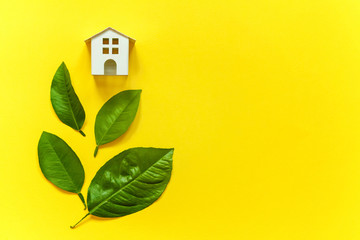 Miniature toy model house with green leaves on yellow colourful trendy backgdrop. Eco Village, abstract environmental background. Real estate mortgage property insurance dream home ecology concept