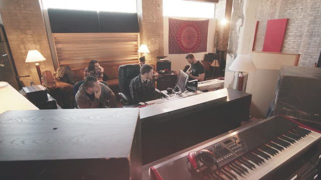 Recording Guitar Track in Studio Move Left. a wide above angle of a group of people and audio engineer listening and tracking guitars in studio moving left