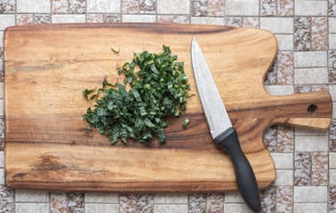 Directly above view of shredded kale with knife on wooden chopping board on tiled kitchen benchtop (selective focus)