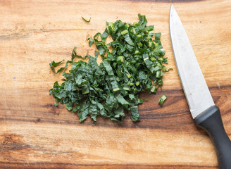 Directly above close up view of shredded kale with knife on wooden chopping board (selective focus)