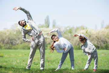 smiling father with daughter and son doing physical exercise on grassy meadow in park