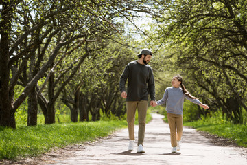 father and daughter holding hands and walking on path in park