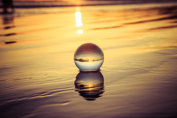 Crystal sphere in water outdoors during sunset, reflecting a beautiful landscape