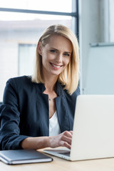 beautiful blonde businesswoman using laptop and smiling at camera