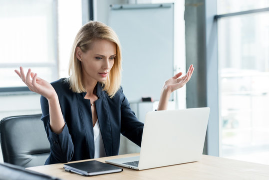 surprised businesswoman gesturing with hands and lookng at laptop in office - Powered by Adobe