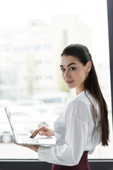 beautiful young businesswoman using laptop and smiling at camera