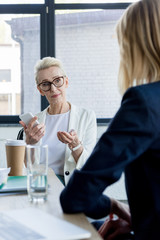 beautiful businesswoman talking at meeting in office and holding smartphone