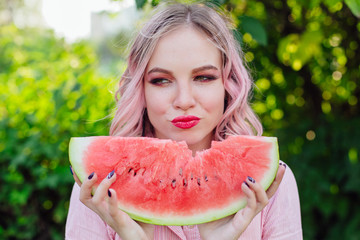 Beautiful young woman with pink hair enjoying watermelon