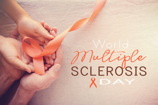 Adult and child hands holding orange Ribbons,  world Multiple sclerosis awareness day