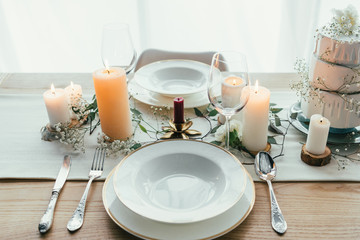 close up view of stylish table setting with candles, wineglasses and wedding cake for rustic wedding