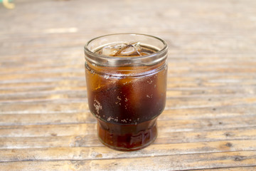 Cola with ice cubes in glass on bamboo table