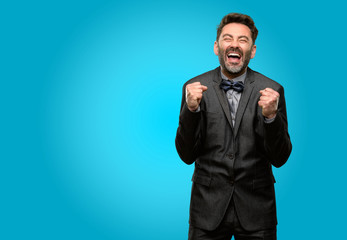 Middle age man, with beard and bow tie happy and surprised cheering expressing wow gesture