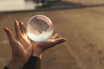 Contact juggling. Hands of a man and a glass ball. Inverted panorama of the city in the reflection of the ball. Mastery of representation. Close-up photo at sunset.