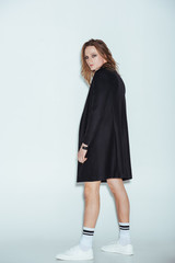 fashionable man posing in long black jacket, on grey