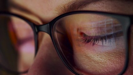 Woman in glasses looking on the monitor and surfing Internet. The monitor screen is reflected in the glasses