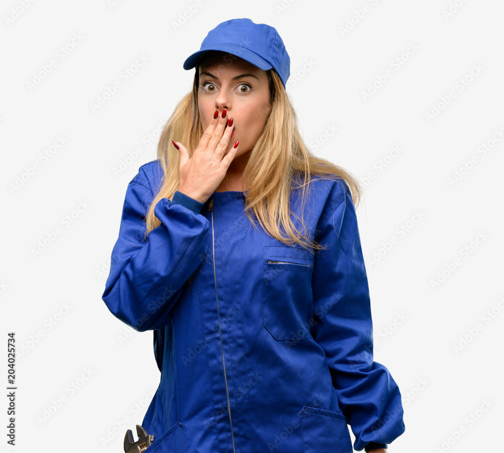 Poster Young plumber woman covers mouth in shock, looks shy, expressing silence and mistake concepts, scared