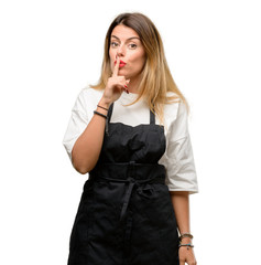 Shop owner woman wearing apron with index finger on lips, ask to be quiet. Silence and secret concept