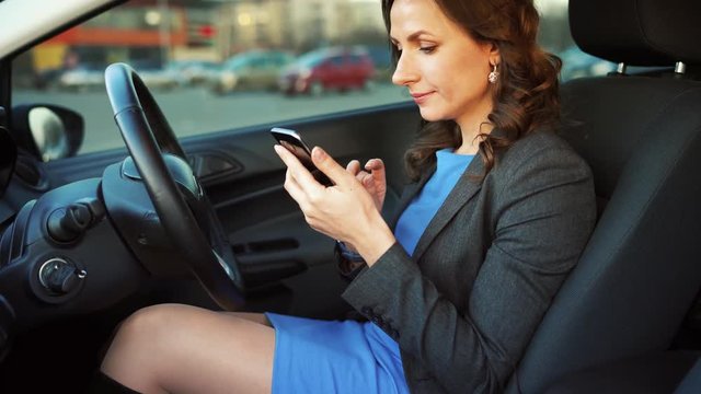 Woman in a blue dress and jacket using a smartphone in the car