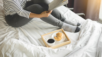 Woman reading book or newspaper and drinking coffee breakfast on bed during the morning