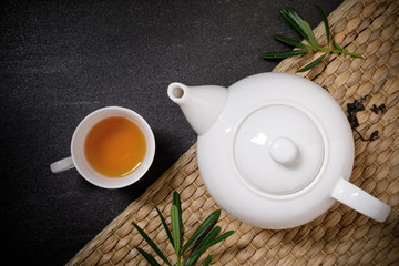 Cup of hot tea with steaming jugs and dry tea on the plate mat on the black stone table background with copyspace for your text.