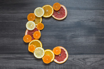 Vitamin c symbol made of sliced orange, grapefruit, mandarin and lemon on the dark wooden background