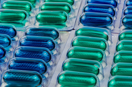 Macro shot detail of blue and green soft gel capsule pills in blister pack. Naproxen and ibuprofen (NSAIDs) : Painkiller medicine. Pharmaceutical packaging industry concept.