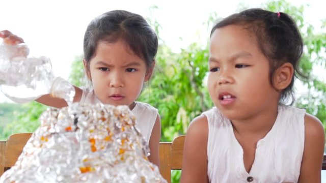 Two asian little girls do the baking soda and vinegar volcano experiment at the table in their house, slow motion in 100 fps