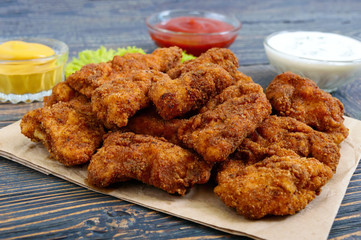 Chicken nuggets. Pieces of deep-fried crispy meat, on paper with different sauces on a wooden table. Traditional snack.
