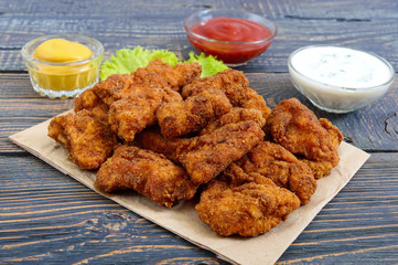 Chicken nuggets. Pieces of deep-fried crispy meat, on paper with different sauces on a wooden...