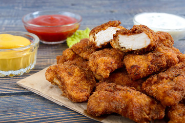 Chicken nuggets. Pieces of deep-fried crispy meat, on paper with different sauces on a wooden table. Traditional snack.