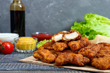 Chicken nuggets. Pieces of deep-fried crispy meat, on paper with different sauces on a wooden table. Traditional snack.