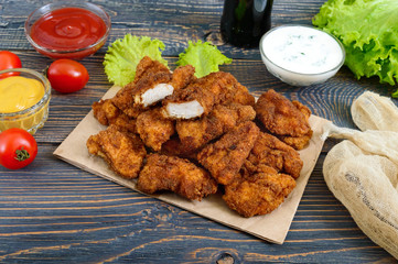 Chicken nuggets. Pieces of deep-fried crispy meat, on paper with different sauces on a wooden table. Traditional snack.