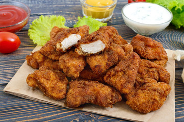 Chicken nuggets. Pieces of deep-fried crispy meat, on paper with different sauces on a wooden table. Traditional snack.