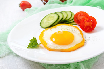Fried egg in a circle of sweet pepper on a white plate with fresh vegetables on a white wooden background. Delicious healthy breakfast. Proper nutrition.