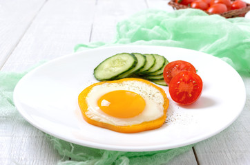 Fried egg in a circle of sweet pepper on a white plate with fresh vegetables on a white wooden background. Delicious healthy breakfast. Proper nutrition.